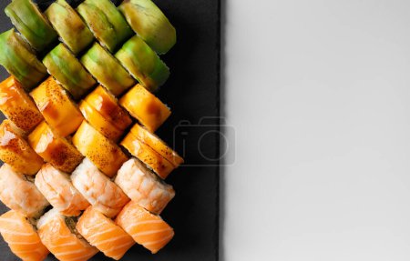 Téléchargez les photos : Un ensemble de rouleaux de sushi multicolores lumineux avec crevettes, saumon, anguille, avocat, fromage dans un emballage en plastique, sur un fond blanc, vue de dessus. Livraison de sushi - en image libre de droit