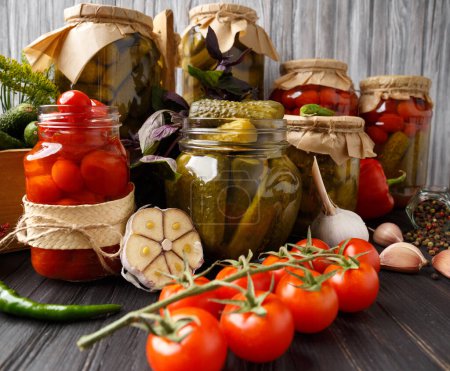 Photo for Canned cherry tomatoes and gherkins in jars, fresh vegetables, spices and herbs for marinade on a wooden background. - Royalty Free Image