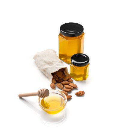 Photo for Almonds in a bag, organic honey in a closed honeycomb glass jars and clear glass bowl and wooden dipper on a white background. A handful of scattered nuts and honey isolated. - Royalty Free Image