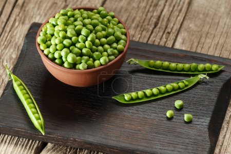 Photo for Fresh organic green peas in closed and open pods, scattered pea seeds, peeled green peas in a clay bowl on a dark wooden board and aged wooden background. vegetable protein. - Royalty Free Image
