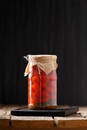 Téléchargez les photos : Tomates cerises marinées dans des bocaux en verre avec couvercles artisanaux sur un fond en bois close-up, espace de copie. - en image libre de droit
