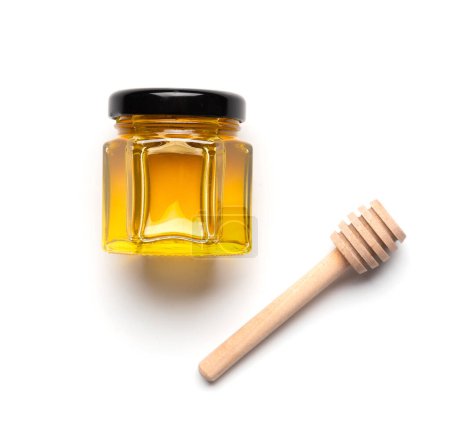 Foto de Miel orgánica en un frasco de vidrio en forma de panales y una cacerola de madera en una vista superior de fondo blanco. La cuchara para la miel y la miel fresca en el frasco al primer plano del aislamiento. Productos saludables. - Imagen libre de derechos