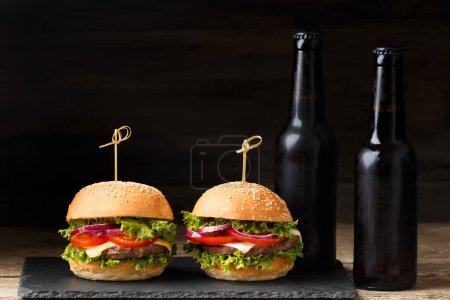 Téléchargez les photos : Deux hamburgers, frites, bière en bouteilles sombres sur fond bois. Restauration rapide, hamburgers faits maison - en image libre de droit