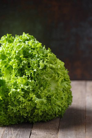 Photo for A large bunch of fresh green lettuce leaves on a wooden table and a dark background. Healthy food, source of minerals and vitamins. - Royalty Free Image