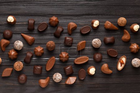 Photo for Different chocolate candies on a dark wooden texture background top view. Assorted sweets on the table. Dark and milk chocolates. Chocolate dessert. Candy flat lay. - Royalty Free Image