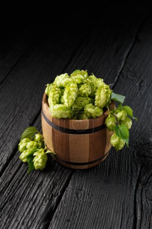 Photo for Green hops in a wooden barrel on a black wooden background, copy space. Brewing traditions. Oktoberfest. Beer Festival. St.Patrick 's Day - Royalty Free Image