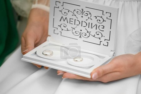 Photo for Wedding rings in a white wedding box with an infinity symbol. The girl's hands hold a box with wedding rings. Accessories for newlyweds. - Royalty Free Image