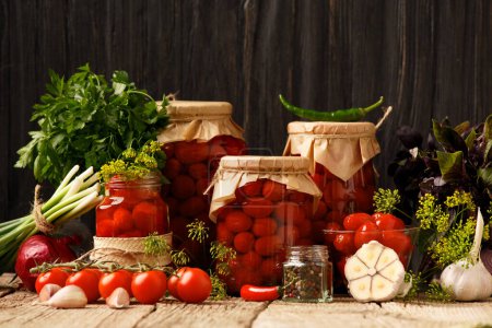 Téléchargez les photos : Tomates cerises en conserve dans un bocal fermé, épices et herbes pour la marinade sur un fond de bois rustique. - en image libre de droit
