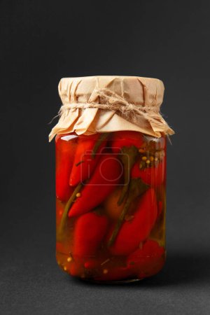Foto de Chiles rojos en escabeche en un frasco de vidrio cerrado aislado sobre un fondo negro. Verduras enlatadas. Snack picante. - Imagen libre de derechos