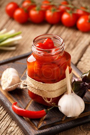Photo for Canned cherry tomatoes in an open glass jar, garlic, chili peppers, fresh tomatoes, spices and herbs for marinade on a wooden background. Pickled vegetables. - Royalty Free Image