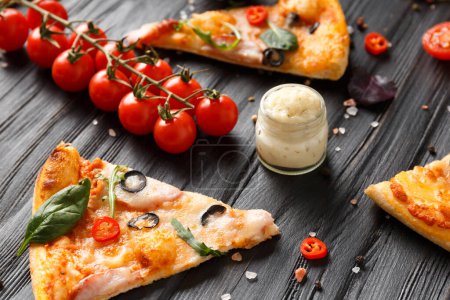 Téléchargez les photos : Des tranches de pizza saccadées, aux olives, au fromage et aux herbes sont disposées sur un fond de bois sombre, une branche de tomates cerises fraîches, des sauces et des assaisonnements pour la pizza. Alimentation italienne. - en image libre de droit