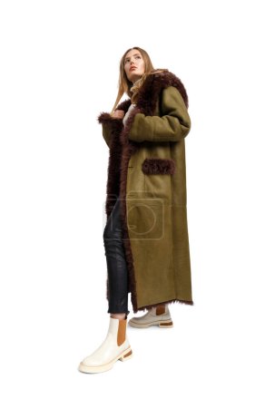 Foto de Una chica joven y elegante en un lujoso abrigo largo de piel de oveja con una capucha de piel y puños posa maravillosamente sobre un fondo blanco. Moda, ropa de abrigo elegante y cómoda, publicidad de ropa. - Imagen libre de derechos