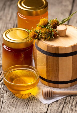 Photo for Honey in transparent bowls, jars, wooden barrel and flowers on a rustic wooden background. Concept of natural organic beekeeping products. - Royalty Free Image