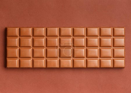 Téléchargez les photos : Grande barre de chocolat entière sur fond brun, vue de dessus. Chocolat au lait isolé. - en image libre de droit
