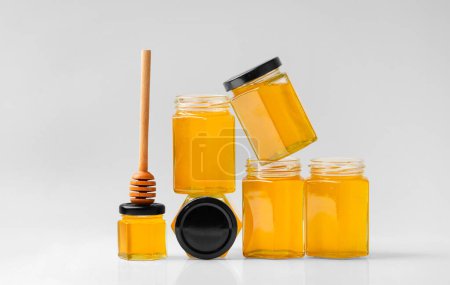 Téléchargez les photos : Composition conceptuelle de bocaux en verre sous forme de nids d'abeilles avec du miel et une trempette en bois sur fond blanc. Composition créative de pots de miel fermés et ouverts les uns sur les autres. - en image libre de droit