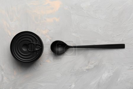 Foto de Lata cerrada redonda mate negra y cuchara negra sobre fondo de textura gris vista superior, conservas, conservas, conservas. - Imagen libre de derechos