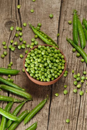 Photo for Fresh organic green peas in closed and open pods, scattered pea seeds, shelled green peas in a clay bowl on an aged wooden background, top view. vegetable protein. - Royalty Free Image
