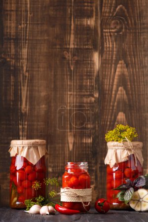 Photo for Canned cherry tomatoes in a closed and open jars, spices and herbs for marinade on a wooden background. - Royalty Free Image