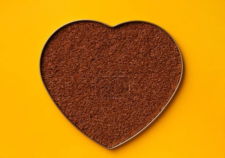 Photo for Heart-shaped box filled with chocolate chips, top view, yellow background. The concept of confectionery, making chocolate, sweets. Postcard, template for Valentine's Day. - Royalty Free Image