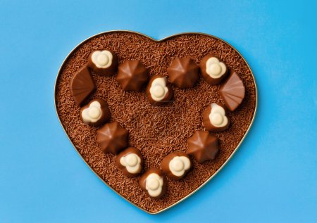 Photo for Heart-shaped box with chocolates and chocolate chips on a blue background, top view. Postcard, template for Valentine's Day. - Royalty Free Image