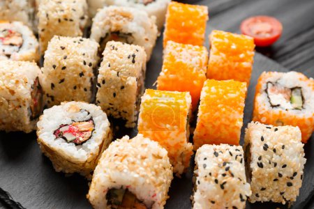 Foto de Conjunto de rollos de sushi con salmón, atún, caviar, semillas de sésamo en un plato de pizarra de piedra negra, primer plano. - Imagen libre de derechos