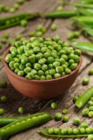 Photo for Fresh organic green peas in closed and open pods, scattered pea seeds, shelled green peas in a clay bowl on an aged wooden background. vegetable protein. - Royalty Free Image