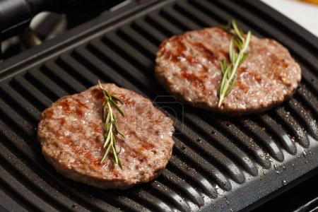 Photo for Beef patties for a burger are fried with spices on a smart electric grill. Cooking homemade hamburgers. Ingredients for burgers. - Royalty Free Image