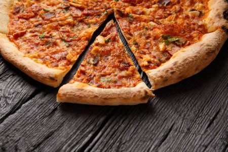 Foto de Pizza con diferentes tipos de carne, cortada en rodajas, una rebanada se separa sobre un fondo de madera negro - Imagen libre de derechos