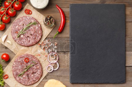Photo for Raw burger patties with spices and rosemary, fresh vegetables, stone plate with space for text on wooden background. - Royalty Free Image