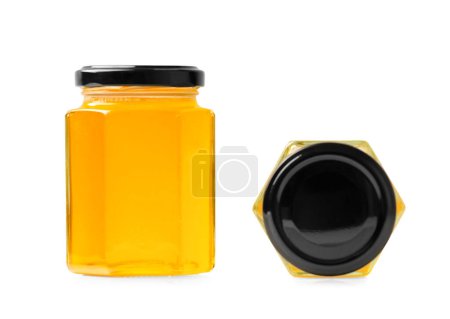 Téléchargez les photos : Composition créative de pots en verre en forme de nid d'abeilles avec du miel fermé avec des couvercles noirs sur un fond blanc gros plan. Pots en verre avec du miel biologique dans différentes positions sur l'isolement. - en image libre de droit