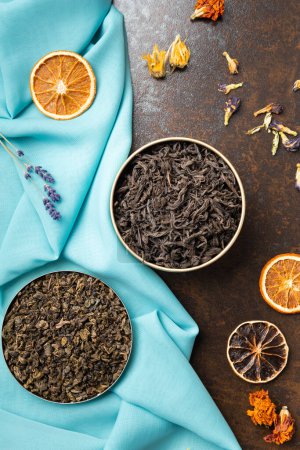 Photo for Composition of black, green, flower tea and dried orange slices on blue and brown backgrounds top view. Large-leaf tea, dried flowers and citrus chips on contrasting backgrounds. - Royalty Free Image