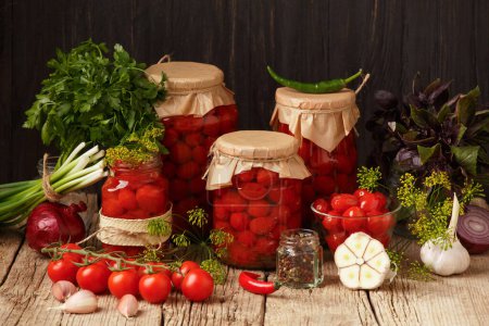 Photo for Homemade canned tomatoes and marinade ingredients. Pickled cherry tomatoes in a closed and open jars, garlic, green onions, basil and spices on an old wooden background - Royalty Free Image