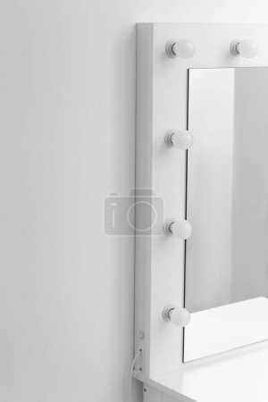 Téléchargez les photos : Partie d'une coiffeuse blanche moderne avec un grand miroir et des lampes contre un mur blanc, gros plan, espace pour le texte. Maquilleur, vestiaire - en image libre de droit