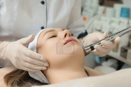 Photo for Rejuvenating facial therapy treatment at spa salon clinic. Young beautiful woman getting lifting anti-aging, face massage and skincare by electroporation facial therapy aesthetic cosmetology. - Royalty Free Image