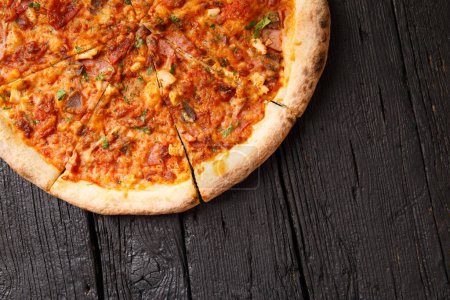 Téléchargez les photos : Pizza italienne avec plusieurs types de viande sur un fond en bois noir, vue du dessus, espace de copie. - en image libre de droit