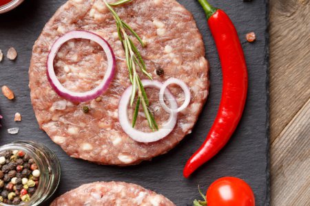 Photo for Raw fresh ground beef burger patties, rosemary, vegetables and spices on a black stone plate on a wooden background, top view, close-up. Ingredients for a hamburger. - Royalty Free Image