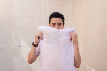 Foto de Los hombres indonesios se sienten perezosos y somnolientos sostienen la almohada con una camiseta blanca. La foto es conveniente utilizar para la publicidad de la expresión del hombre y el estilo de vida de la manera. - Imagen libre de derechos