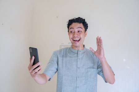 Moslem asiatischen Mann glücklich während Videoanruf mit Smartphone, wenn Ramadan-Feier. Das Foto eignet sich für Ramadhan-Plakate und Medien mit muslimischen Inhalten.