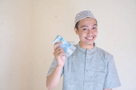 Téléchargez les photos : Musulman Asiatique heureux, souriant quand a eu THR argent Ramadan célébration. La photo est appropriée pour l'affiche Ramadhan et les médias de contenu musulman. - en image libre de droit