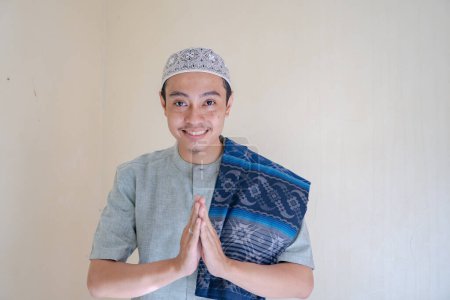 Téléchargez les photos : Homme musulman asiatique saluant geste avec sourire lors de la célébration du Ramadan. La photo est appropriée pour l'affiche Ramadhan et les médias de contenu musulman. - en image libre de droit