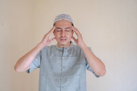 Téléchargez les photos : Homme musulman asiatique vertigineux et mal de tête face à la célébration du Ramadan. La photo est appropriée pour l'affiche Ramadhan et les médias de contenu musulman. - en image libre de droit