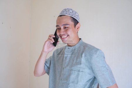Téléchargez les photos : Homme musulman asiatique appelant avec smartphone avec visage heureux lors de la célébration du Ramadan. La photo est appropriée pour l'affiche Ramadhan et les médias de contenu musulman. - en image libre de droit