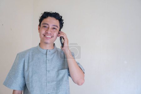 Ein muslimischer Asiate telefoniert während des Ramadan mit einem Smartphone mit glücklichem Gesicht. Das Foto eignet sich für Ramadhan-Plakate und Medien mit muslimischen Inhalten.