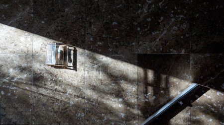 Foto de Wall tiled with marble and with an unlit lamp on which a ray of sunlight falls. - Imagen libre de derechos