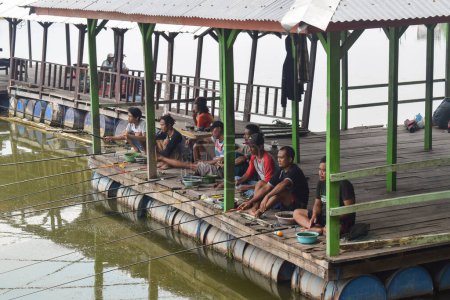 Foto de Pasuruan - November 17, 2022 : A group of men fishing together with net and rod sitting on the wooden pier during the morning on the lake - Imagen libre de derechos