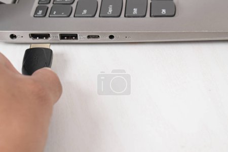 Foto de El hombre está conectando el cable HDMI negro en el puerto HDMI de la computadora portátil moderna en fondo blanco - Imagen libre de derechos
