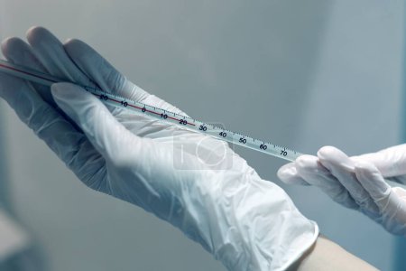 Téléchargez les photos : Gloved hands holding thermometer in the laboratory - en image libre de droit