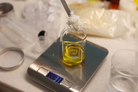 Téléchargez les photos : Put an ingredient in the beaker, weigh jojoba oil in the beaker on the electronic scale, spoon the ingredient laboratory - en image libre de droit