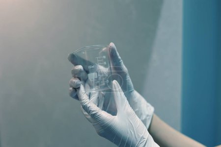 Téléchargez les photos : Gloved hands holding an empty beaker in the laboratory - en image libre de droit