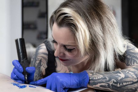 Horizontal photo with a serene expression, a tattoo artist is fully immersed in inking a complex design, showcasing her innate talent and steady hand. Concept business, art.